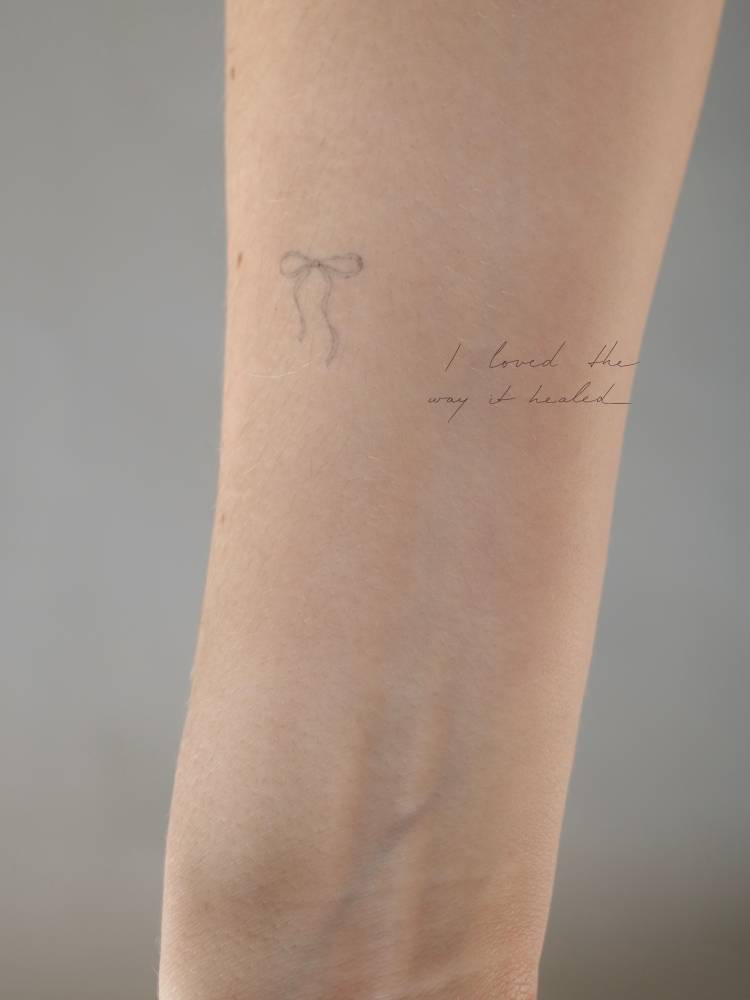 Healed bow tattoo in fine line style located on the inner forearm.