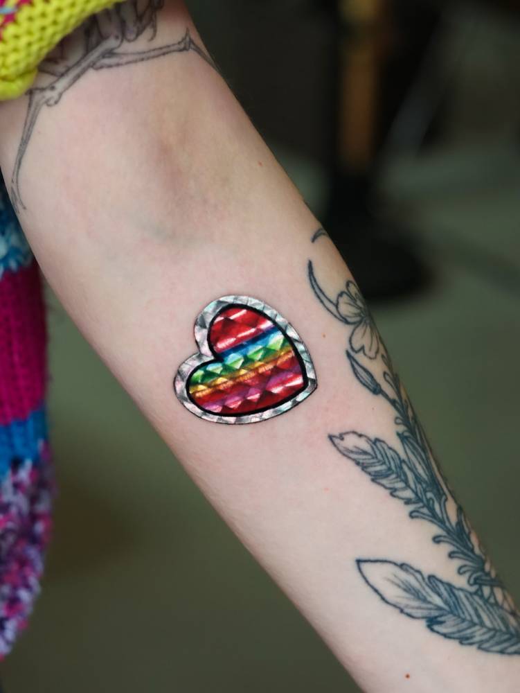 Holographic heart sticker tattooed on the inner forearm.
