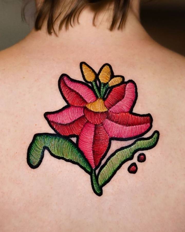 Embroidery style lily flower patch tattoo located on the upper back.