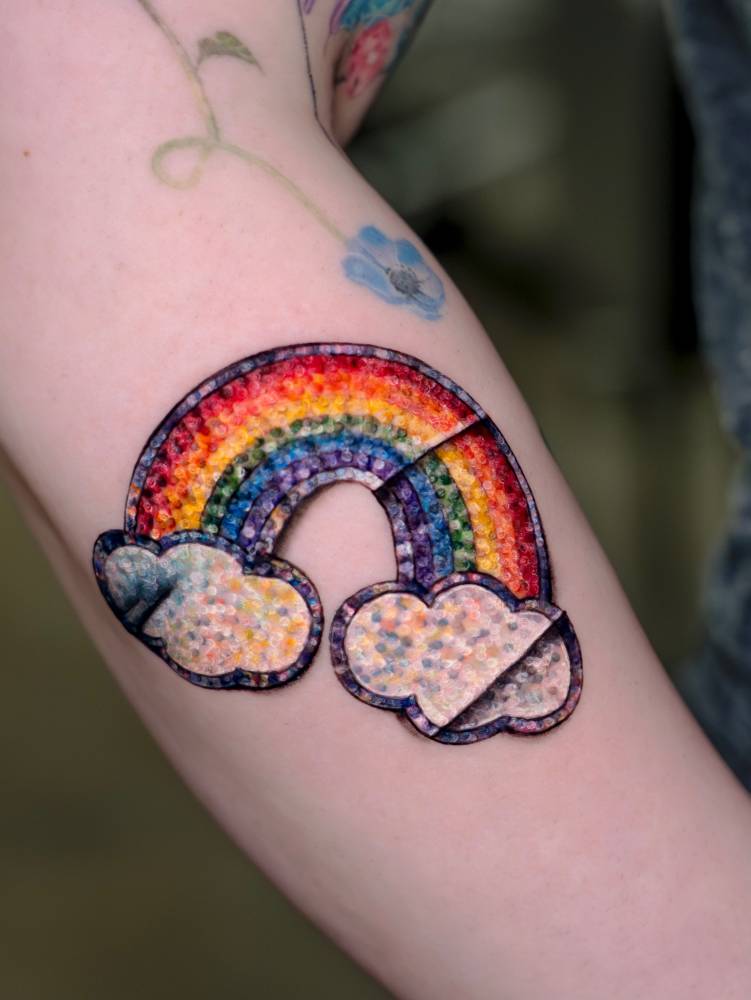 Realistic rainbow sticker tattoo located on the forearm.