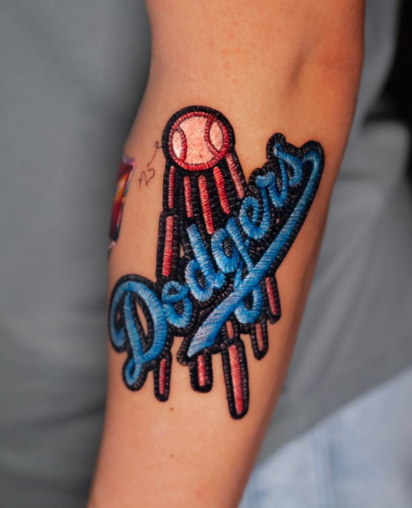 LA Dodgers patch tattoo in embroidery style located on the forearm.