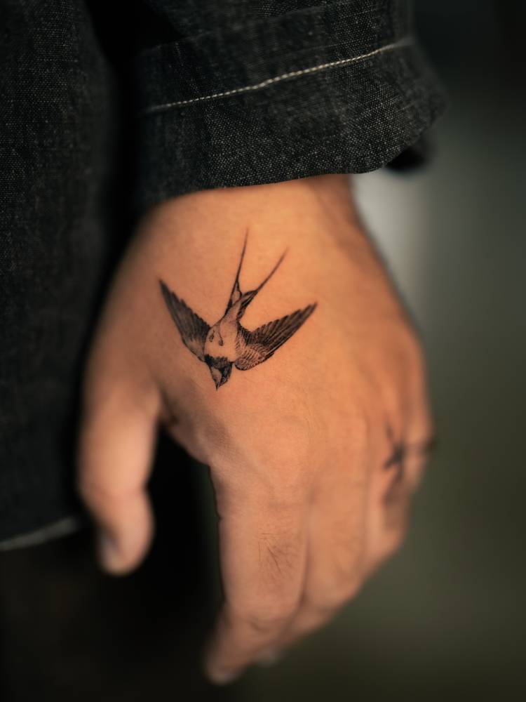 Little swallow tattoo located on the hand, micro-realistic style.