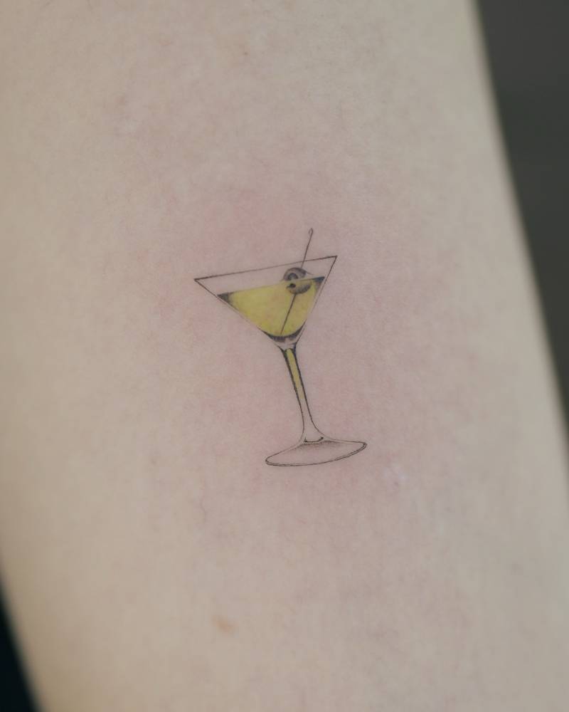 Martini cocktail tattoo placed on the upper arm, micro-realistic style.
