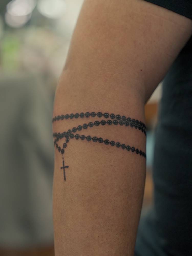 Rosary tattoo in micro-realistic style located on the forearm.
