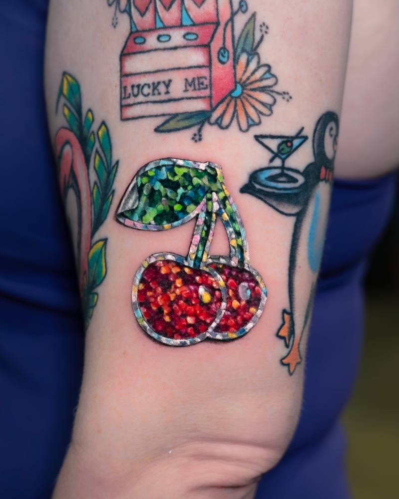 Sparkling cherry sticker tattooed on the upper arm.
