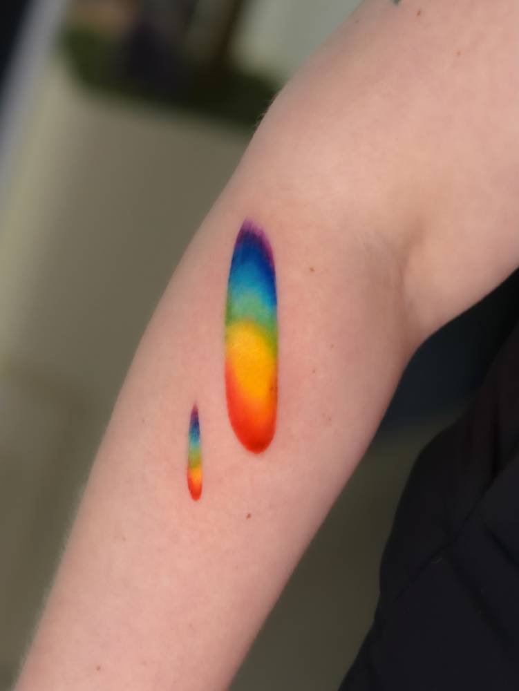 Watercolor style visible spectrum tattoo located on the forearm.