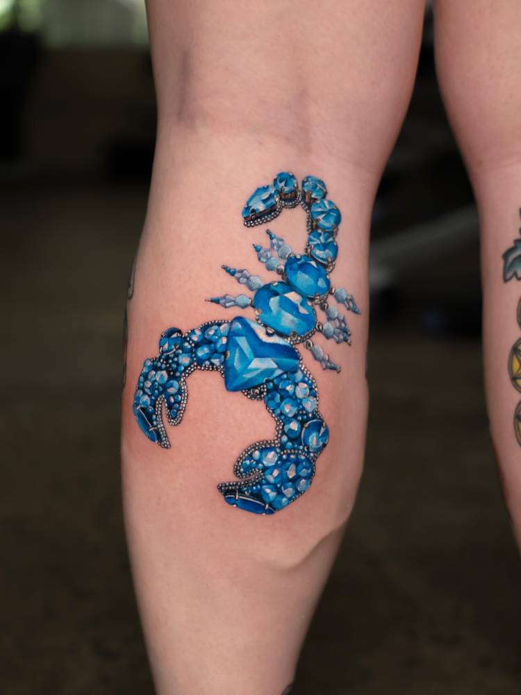 Scorpion jewellery tattoo located on the calf, realistic style.