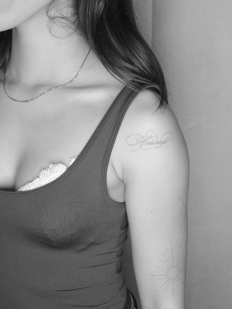 Script font word "heavenly" tattooed on the shoulder.