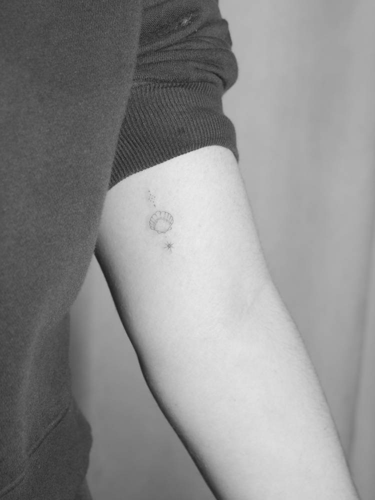 Scallop shell tattoo located on the inner arm, fine line style.