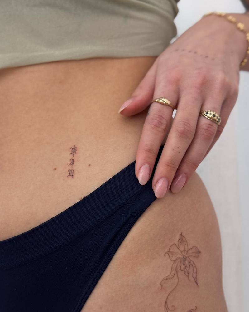 Gothic style initials tattoo located on the waist.
