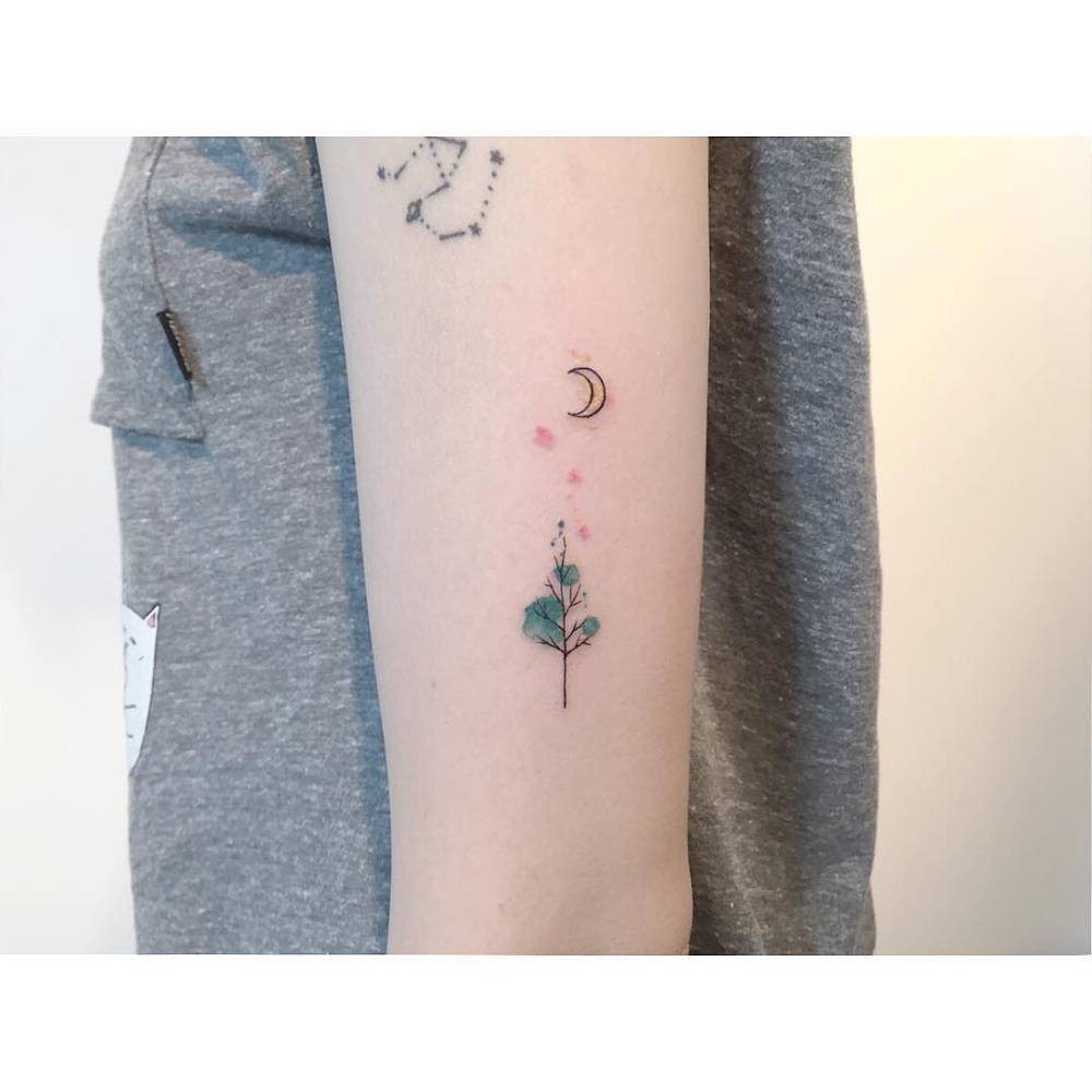 Pine tree and moon tattoo in minimalistic style located on the upper arm.