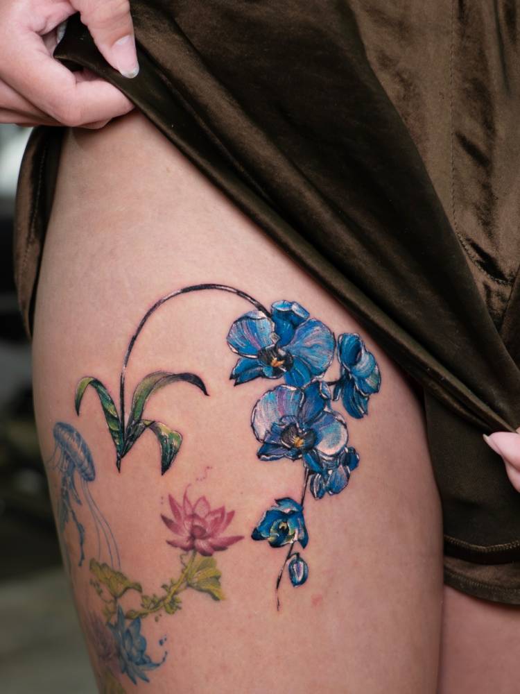 Blue Orchids in realistic style tattooed on the thigh.