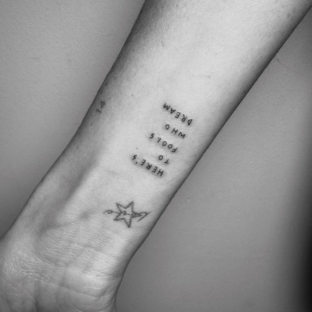 "Here's to fools who dream" lettering tattoo handwritten on the wrist.