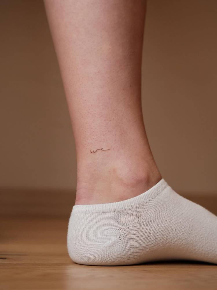 Handwritten font word "we" tattooed on the ankle.