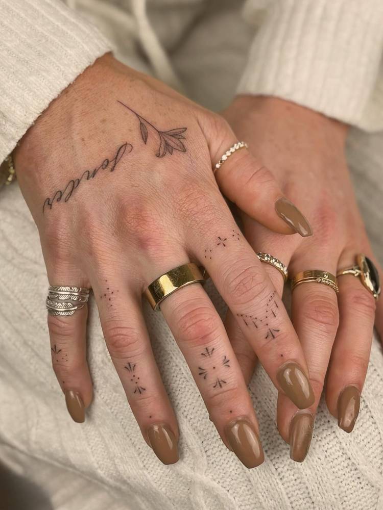 Word "sonder", flower and ornaments tattooed on the hand.