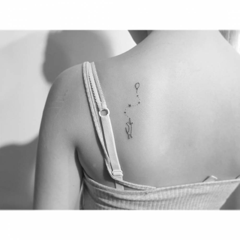 Cat and balloon tattoo in minimalistic style located on the shoulder blade.
