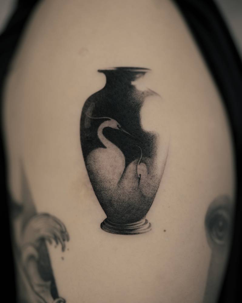 Vase and heron tattoo in micro-realistic style located on the upper arm.