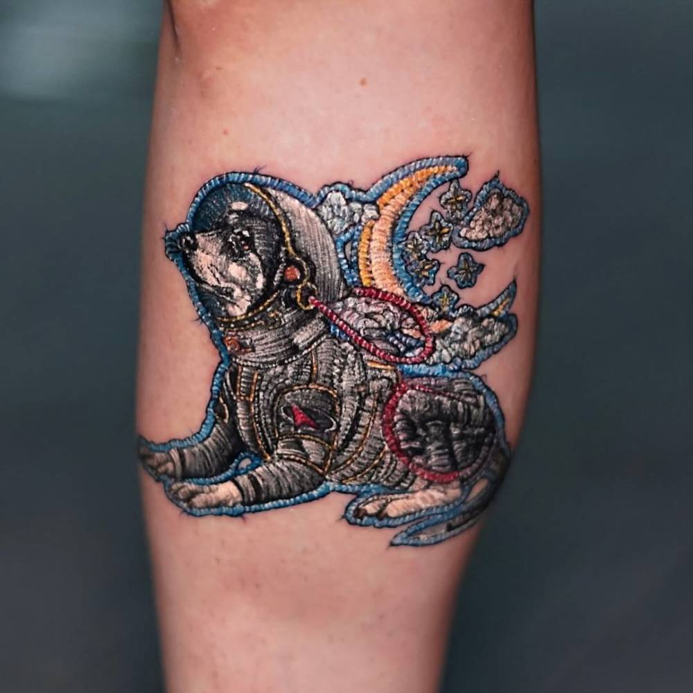 Astronaut dog patch tattoo in embroidery style located on the calf.