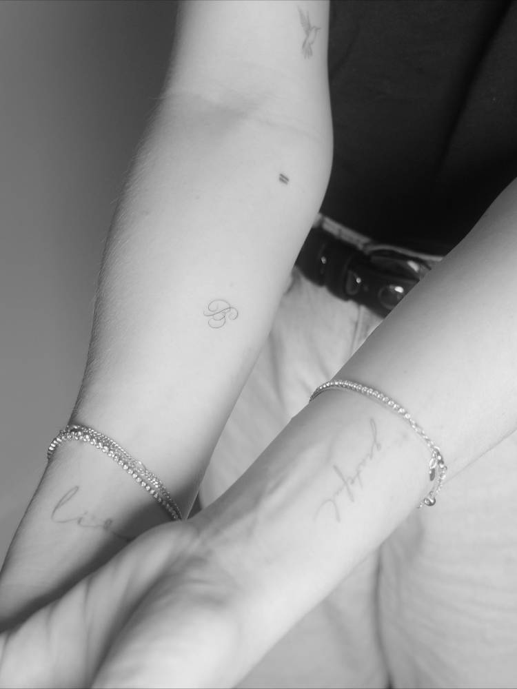 Script font letter "B" tattoo located on the inner forearm.