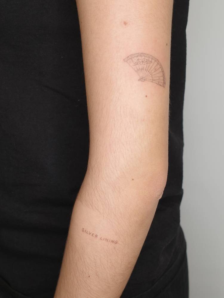Hand fan and "silver lining" tattoos located on the arm.