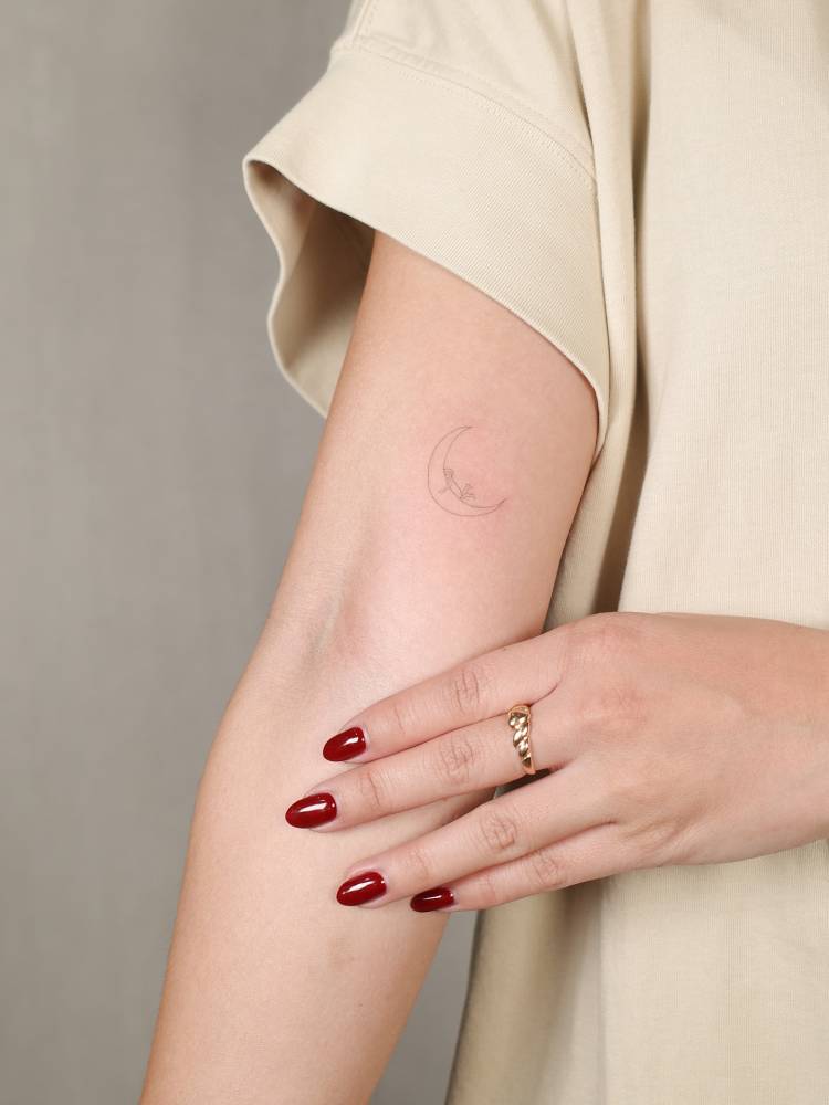 Hugging the moon tattoo in fine line style located on the inner arm.