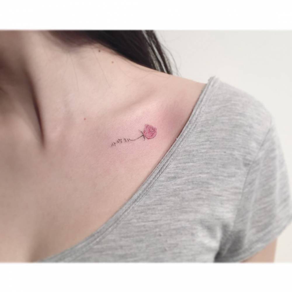 Pink rose and korean lettering tattoo located on the collarbone.