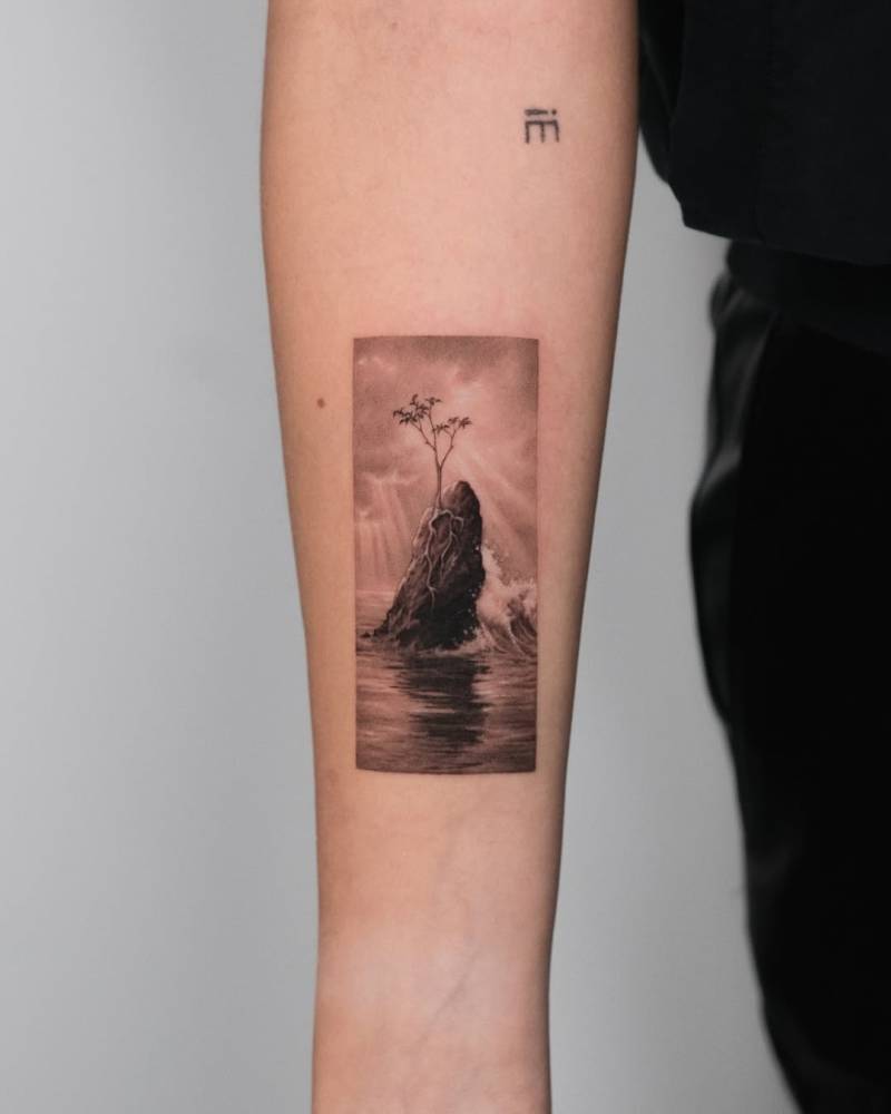 Tree growing on top of a rock tattooed on the inner forearm.