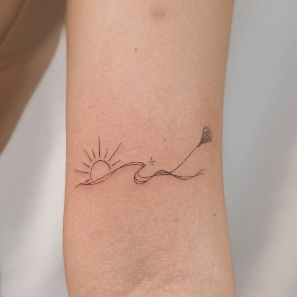 Parasailing tattoo located on the bicep, fine line style.