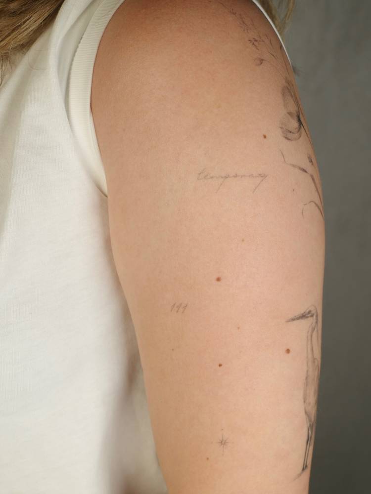 Healed word "temporary" and number "111" tattoos located on the upper arm.