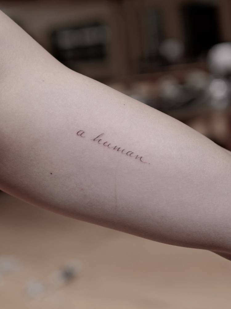 "A human" lettering tattoo located on RM's inner arm.