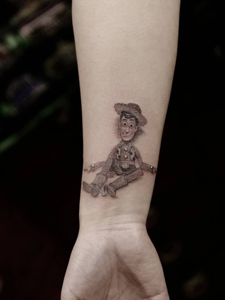 Woody tattoo in cartoon style located on the wrist.