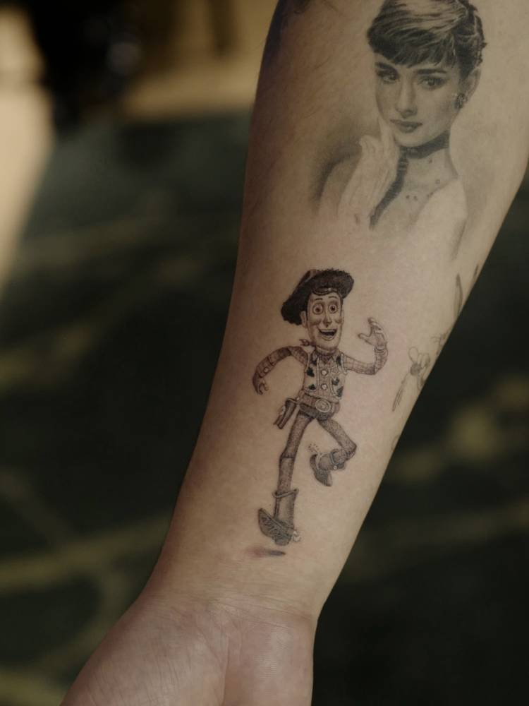 Woody tattoo in cartoon style located on the wrist.
