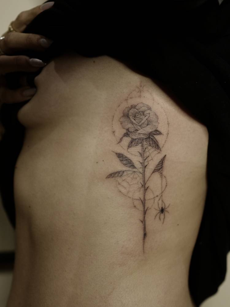 Single needle rose and spider tattoo located on the rib.