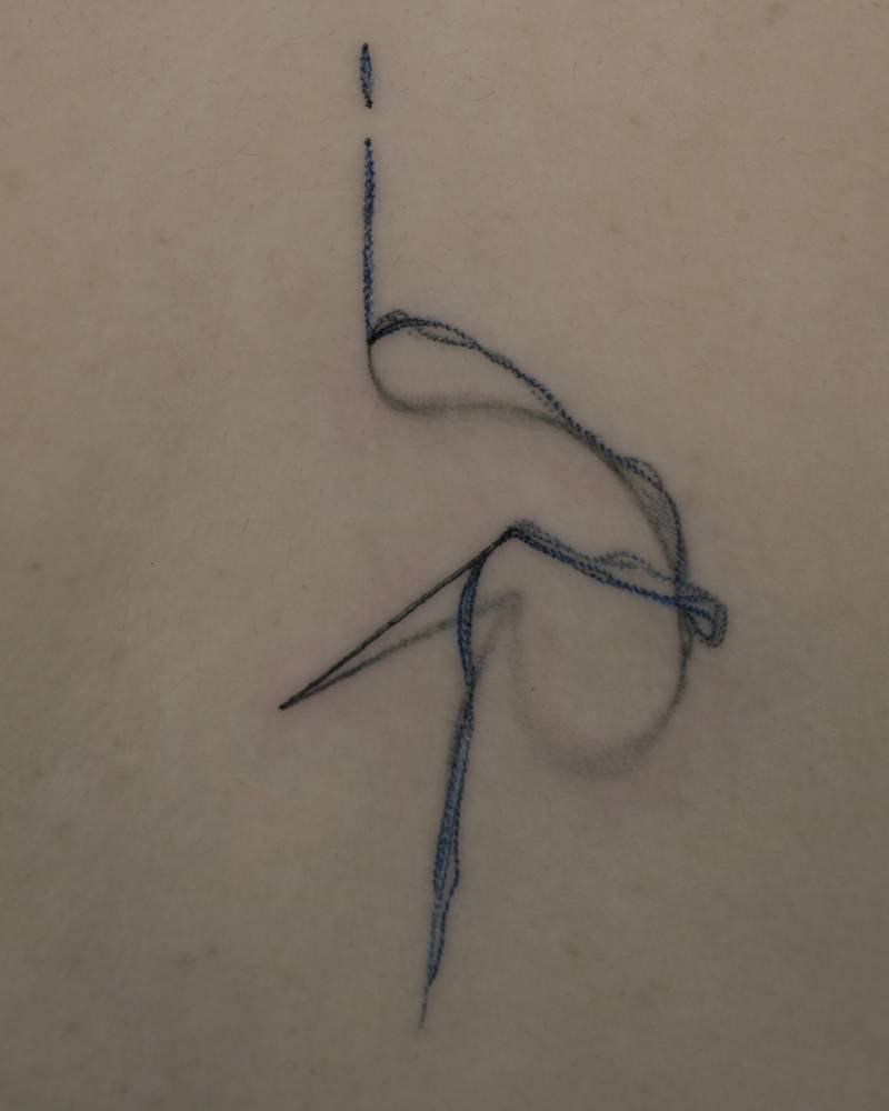 Thread and needle tattoo located on the back, realistic style.
