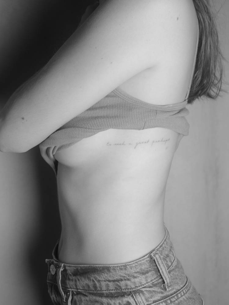 "To seek a great perhaps" lettering tattoo located on the side boob.