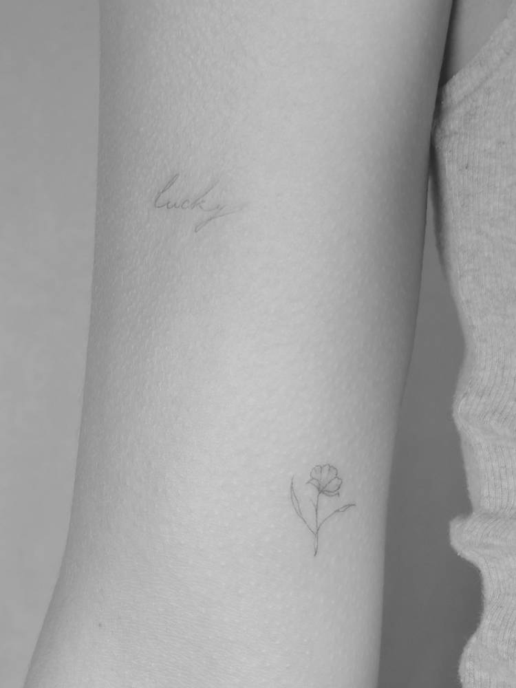 Handwritten font word "lucky" and little flower tattooed on the inner arm.