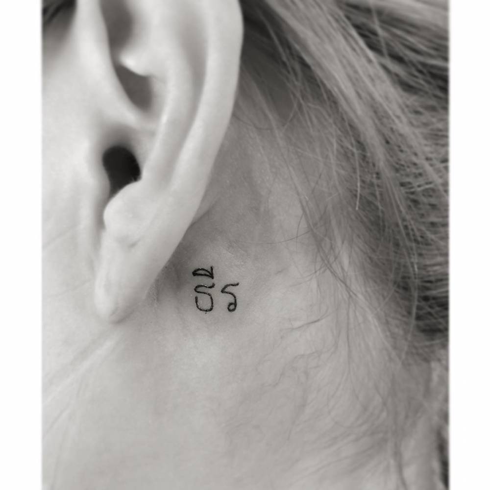 Tiny Thai lettering tattoo located behind the ear.