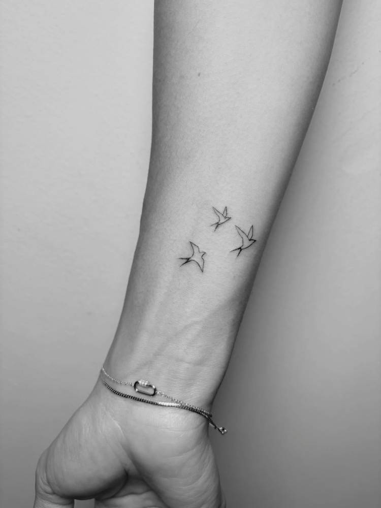 Flying swallows tattoo in fine line style located on the wrist.
