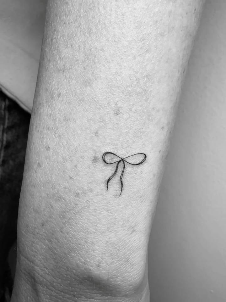 Bow tattoo in illustrative style located on the wrist.