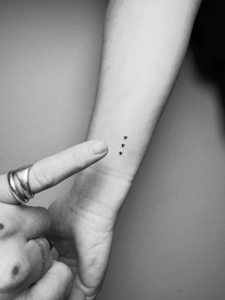 Three little hearts tattoo located on the wrist, minimalist style.