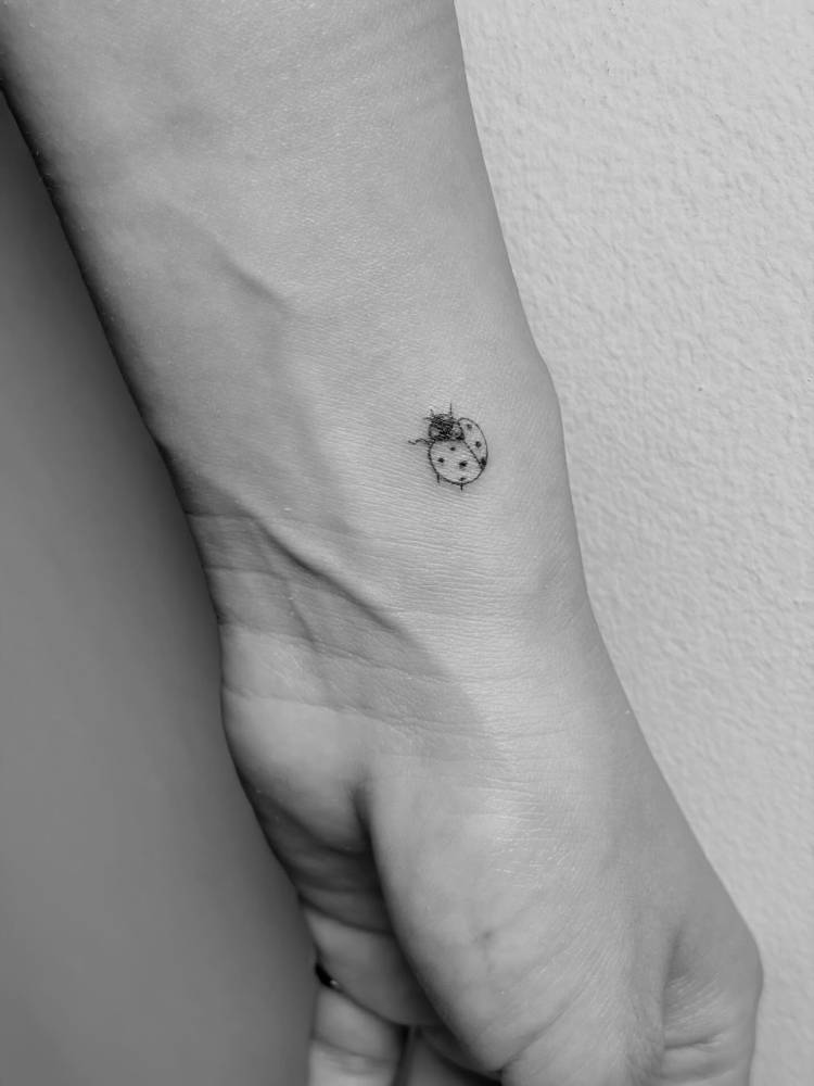 Little ladybug tattoo in minimalist style located on the wrist.