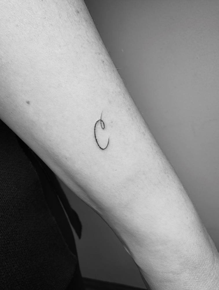 Script font letter "C" tattoo placed on the wrist.