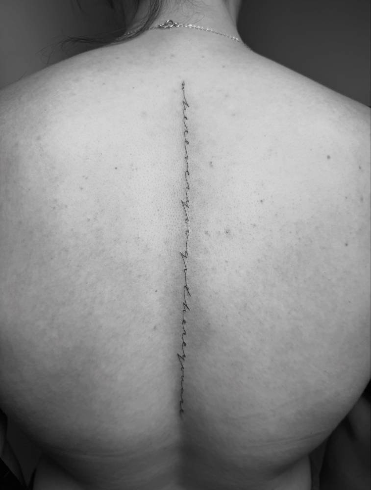 "Wherever you go, there you are" lettering tattoo located on the spine.