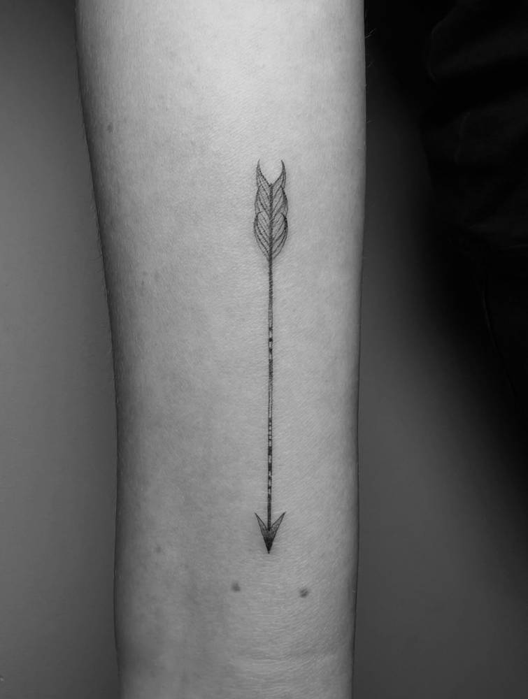 Arrow tattoo in illustrative style located on the wrist.