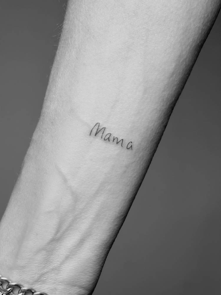 Handwritten font word "mama" tattooed on the wrist.