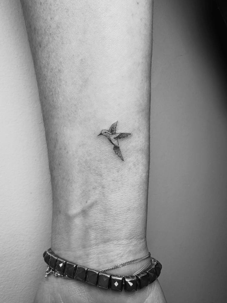 Hummingbird tattoo located on the wrist, illustrative style.