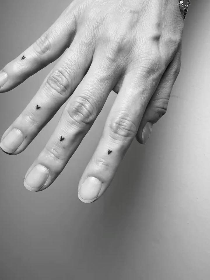 Tiny hearts tattooed on the fingers, done in minimalist style.