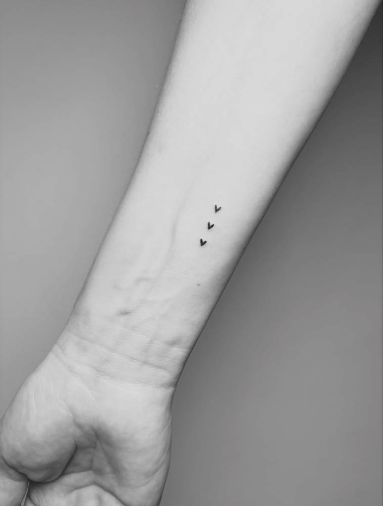 Tiny three hearts tattoo placed on the wrist, minimalist style.