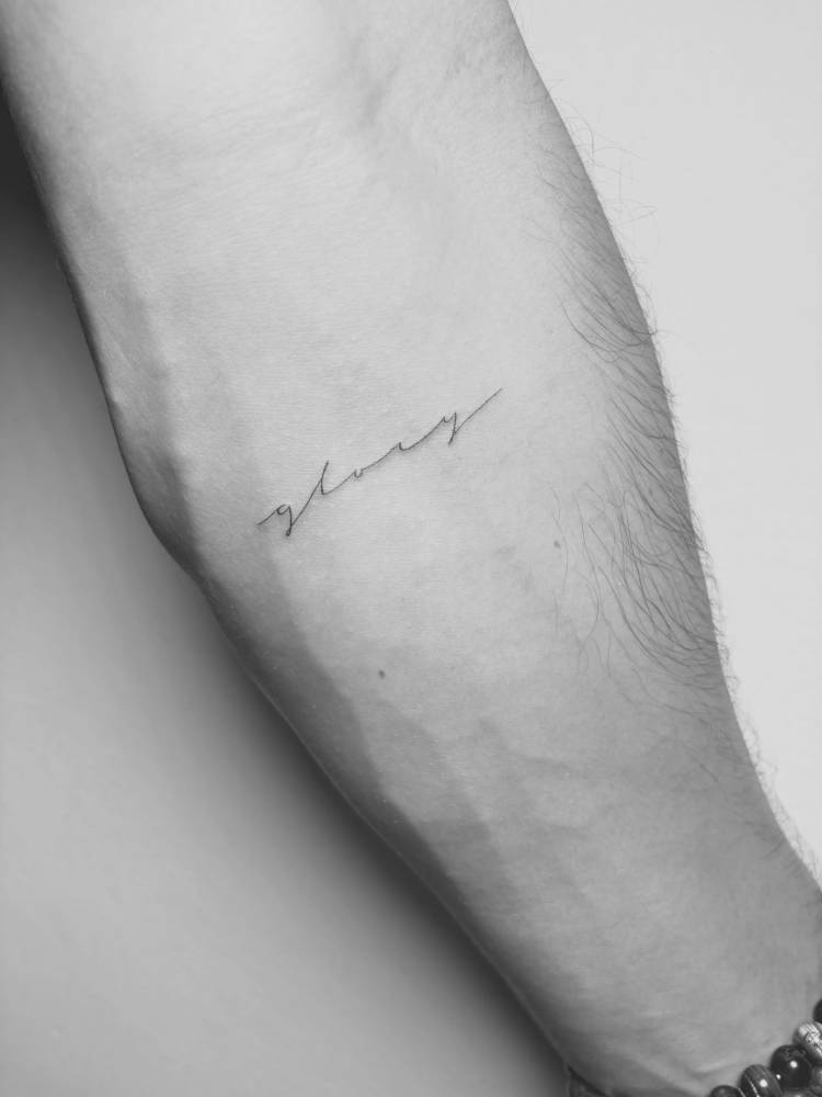 Lettering tattoo of the word "glory" located on the inner forearm.