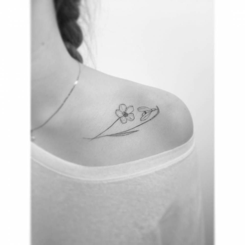 Little flowers tattooed on the collarbone, fine line style.